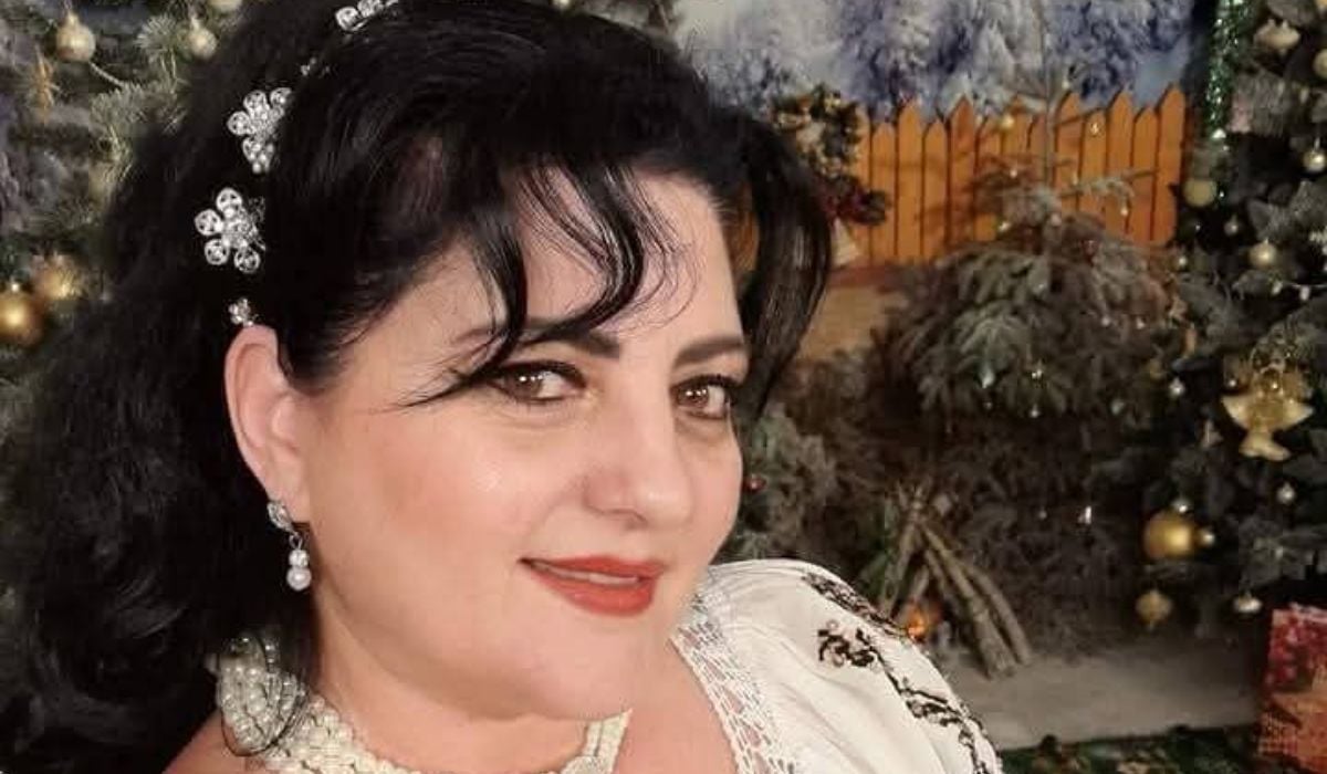 Imagine de prim plan cu Mihaela Cojocaru, cu o bentiță cu flori în păr, iar pe fundal un decor de Crăciun